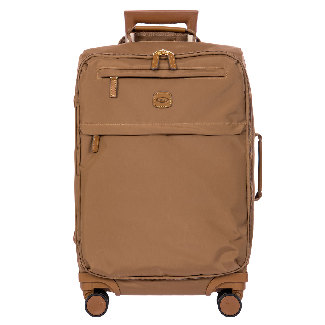 A brown softside spinner suitcase with a telescoping handle extended, shown against a plain white background. The suitcase features a textured fabric body, a front zippered pocket, and a small oval logo patch on the front.