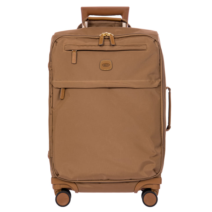A brown softside spinner suitcase with a telescoping handle extended, shown against a plain white background. The suitcase features a textured fabric body, a front zippered pocket, and a small oval logo patch on the front.