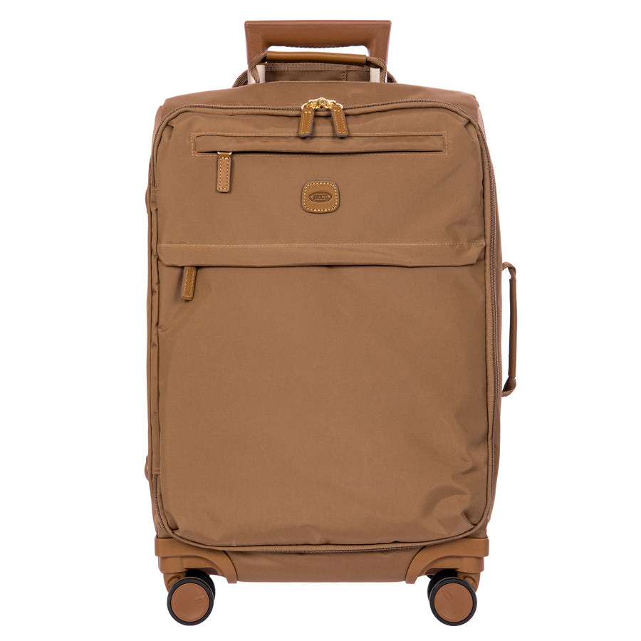 A brown softside spinner suitcase with a telescoping handle extended, shown against a plain white background. The suitcase features a textured fabric body, a front zippered pocket, and a small oval logo patch on the front.