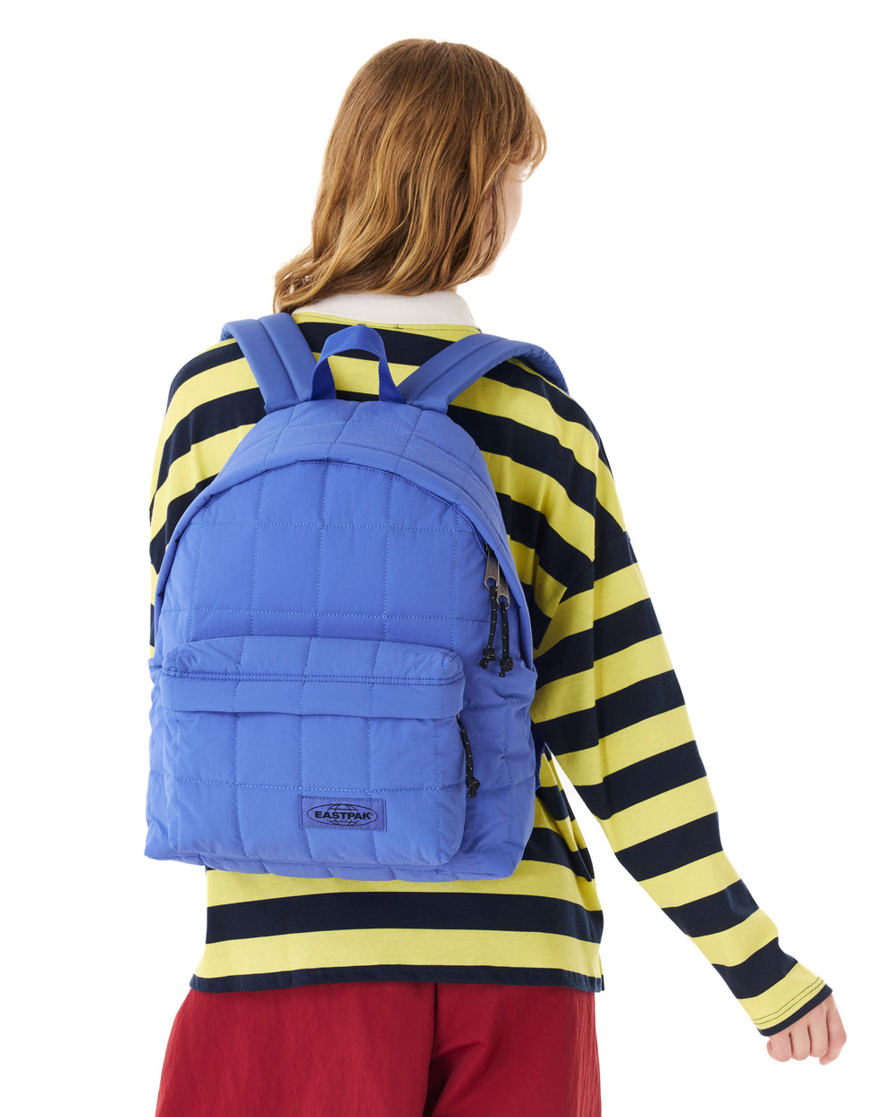 A person shown from the back wearing a bright blue quilted backpack over a yellow and navy striped long-sleeve shirt, against a plain white background.