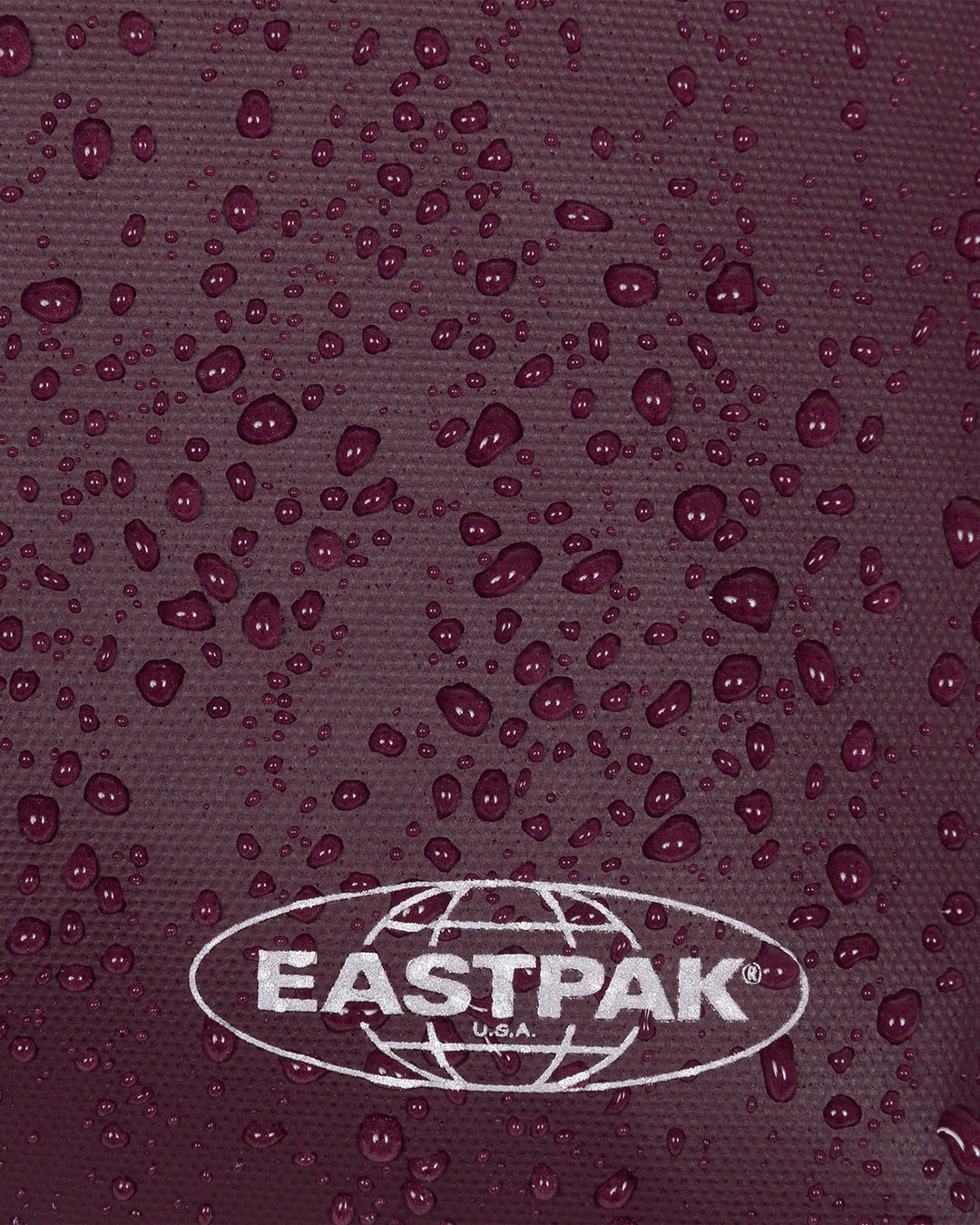 Close-up of a dark plum textured fabric covered with water droplets, featuring a white Eastpak logo at the bottom.