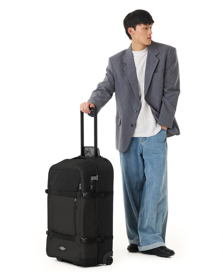 Man in gray blazer and blue jeans holding a black suitcase on a white background