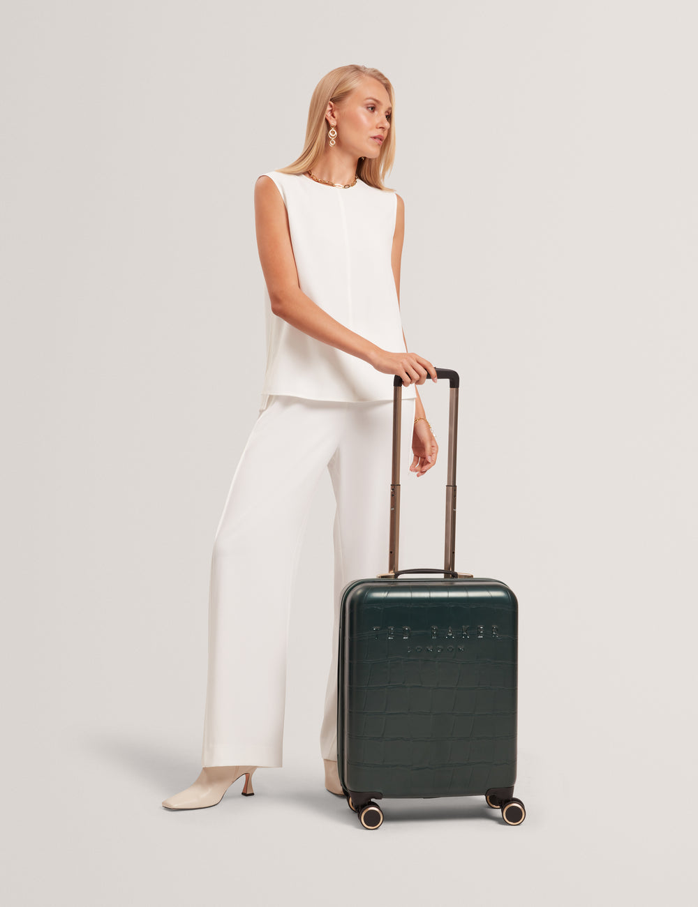 Model holding a green suitcase against a plain background