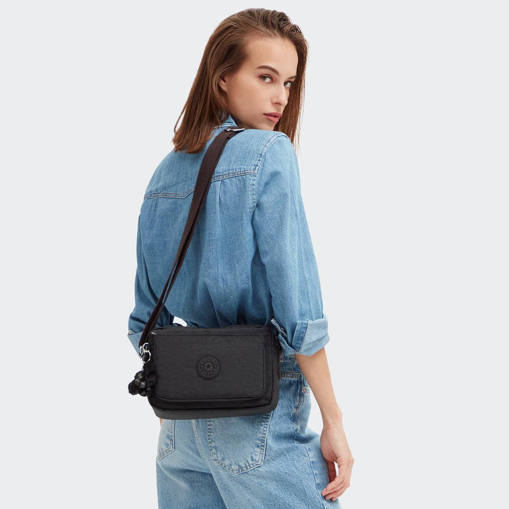 Woman wearing a black crossbody bag with a white background