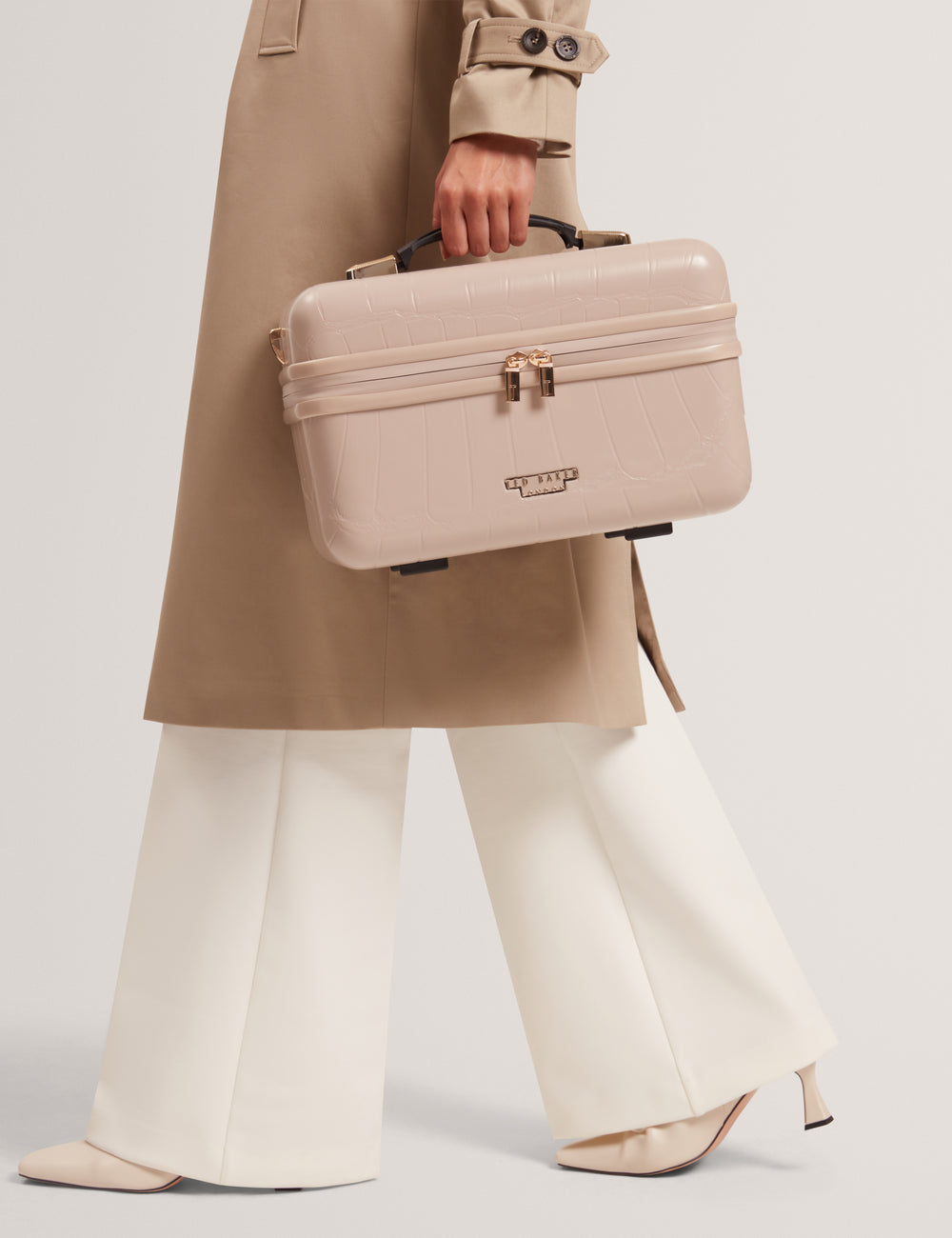 Model holding a beige Ted Baker London vanity case against a plain background