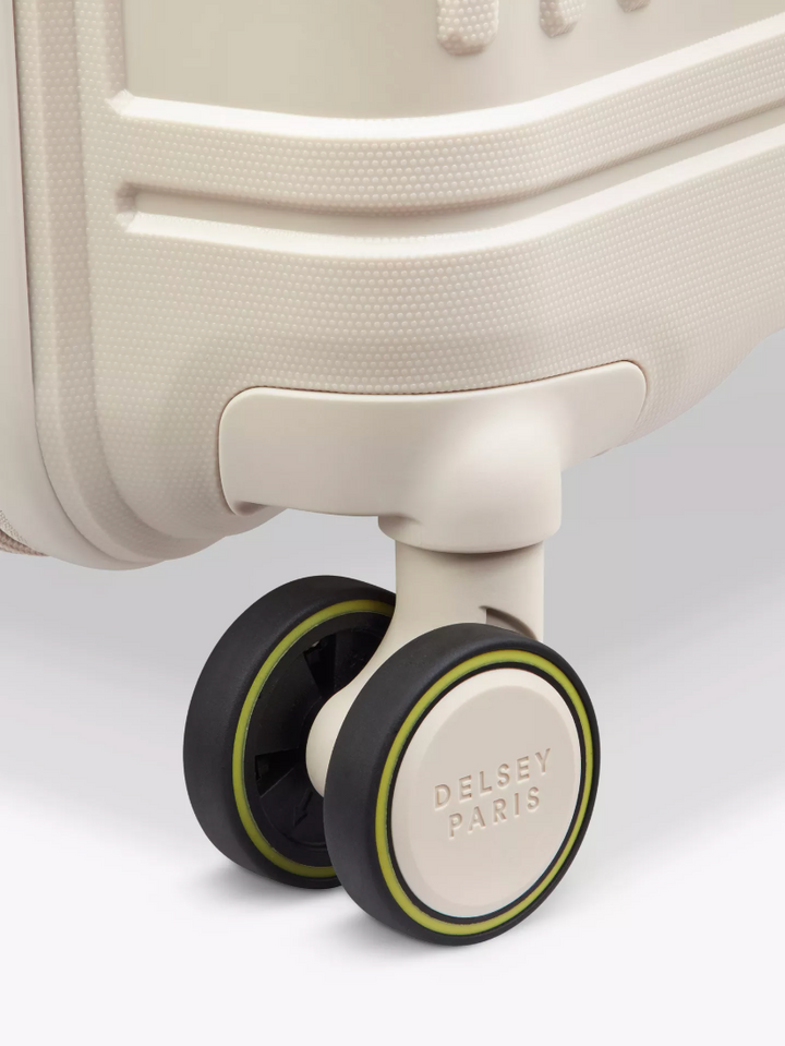 Close-up of a beige Delsey Paris suitcase with wheels on a light gray background