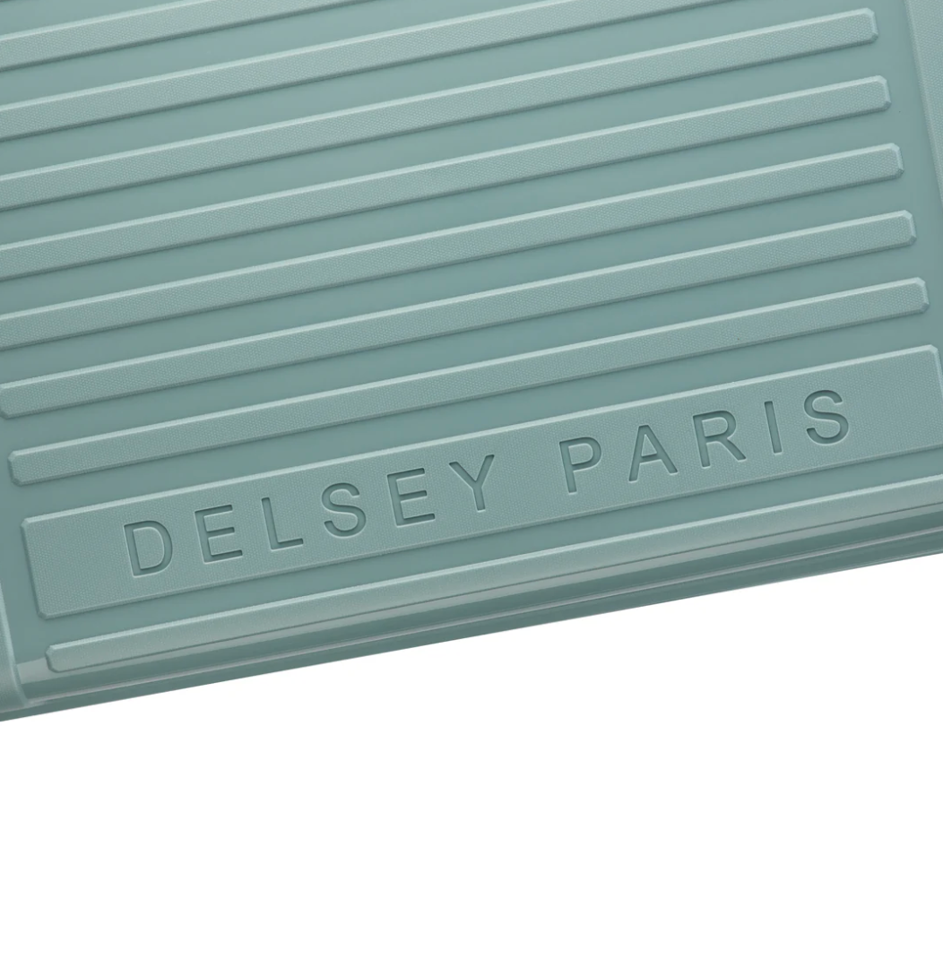 Close up of a sage green suitcase with 'Delsey Paris' branding on a white background
