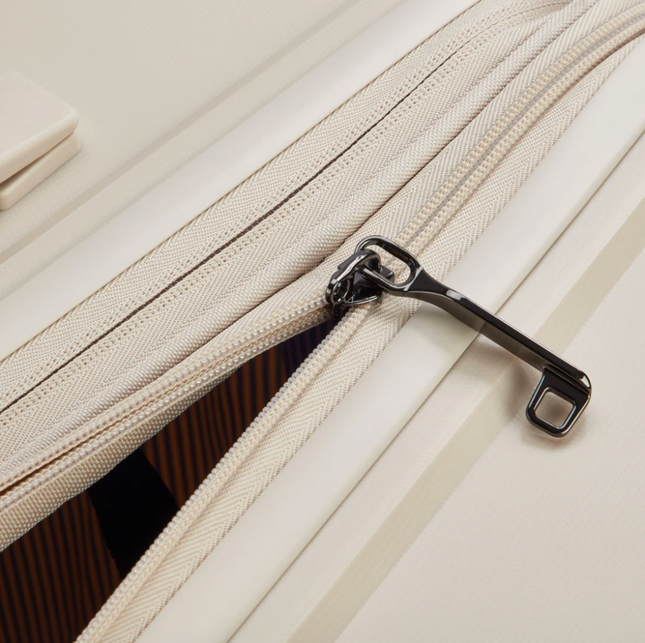 Close-up of a beige Delsey suitcase with the zipper and expansion