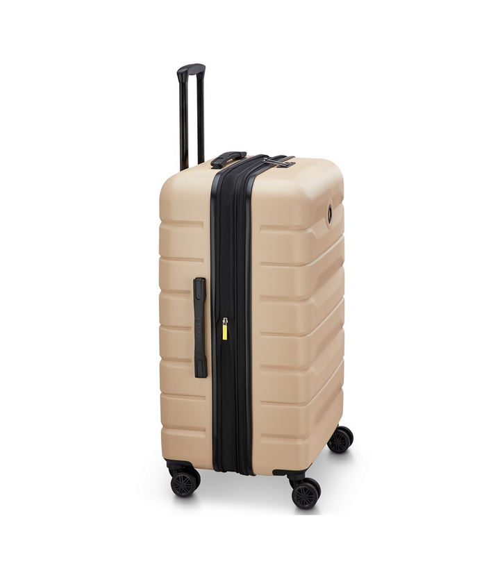 Side angle of a Beige Delsey suitcase with expansion, a black handle and wheels on a white background