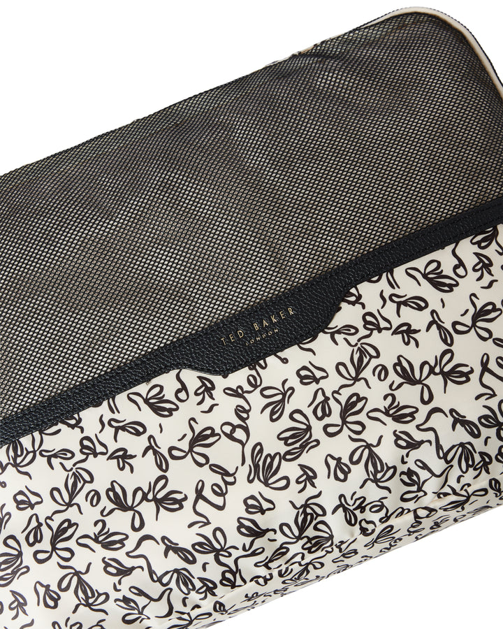 Close up of a Ted Baker packing cube with Ted Baker branding and breathable mesh. Lining print is black ribbon design on cream on a white background