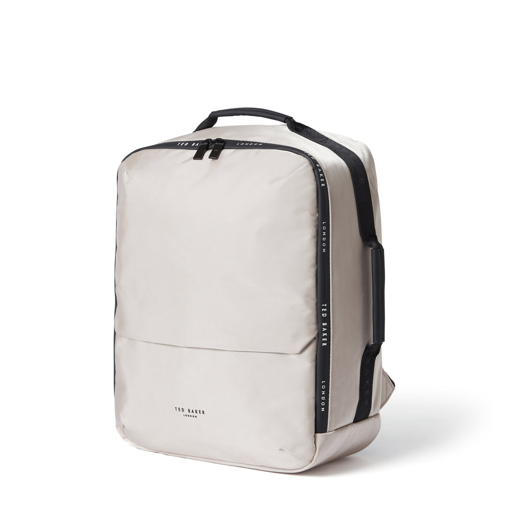 A light beige backpack by Ted Baker London with black accents, including a top handle, side straps, and vertical branding text, shown on a clean white background.