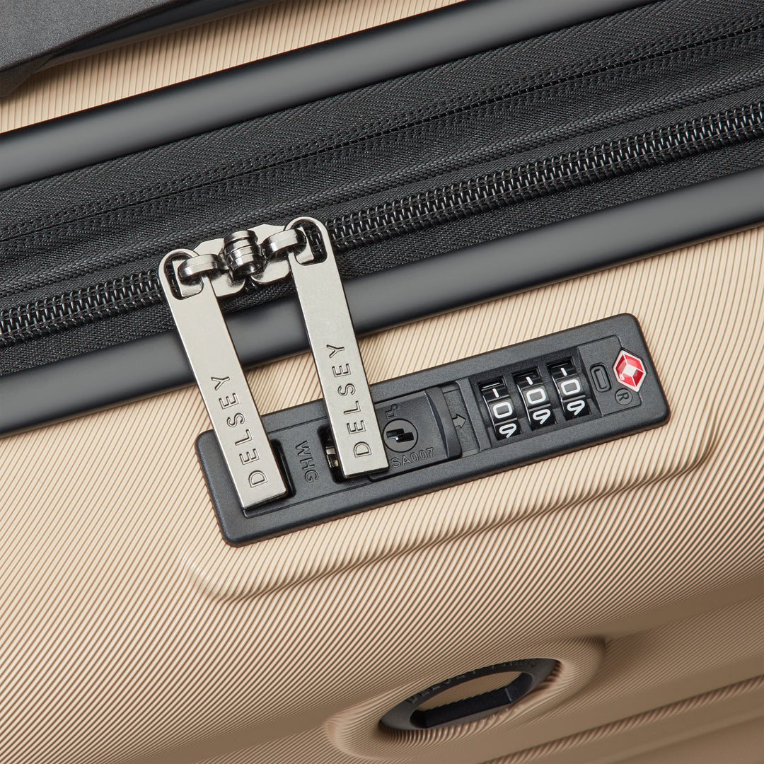 Close-up of a beige suitcase with a black zipper and Delsey brand lock.