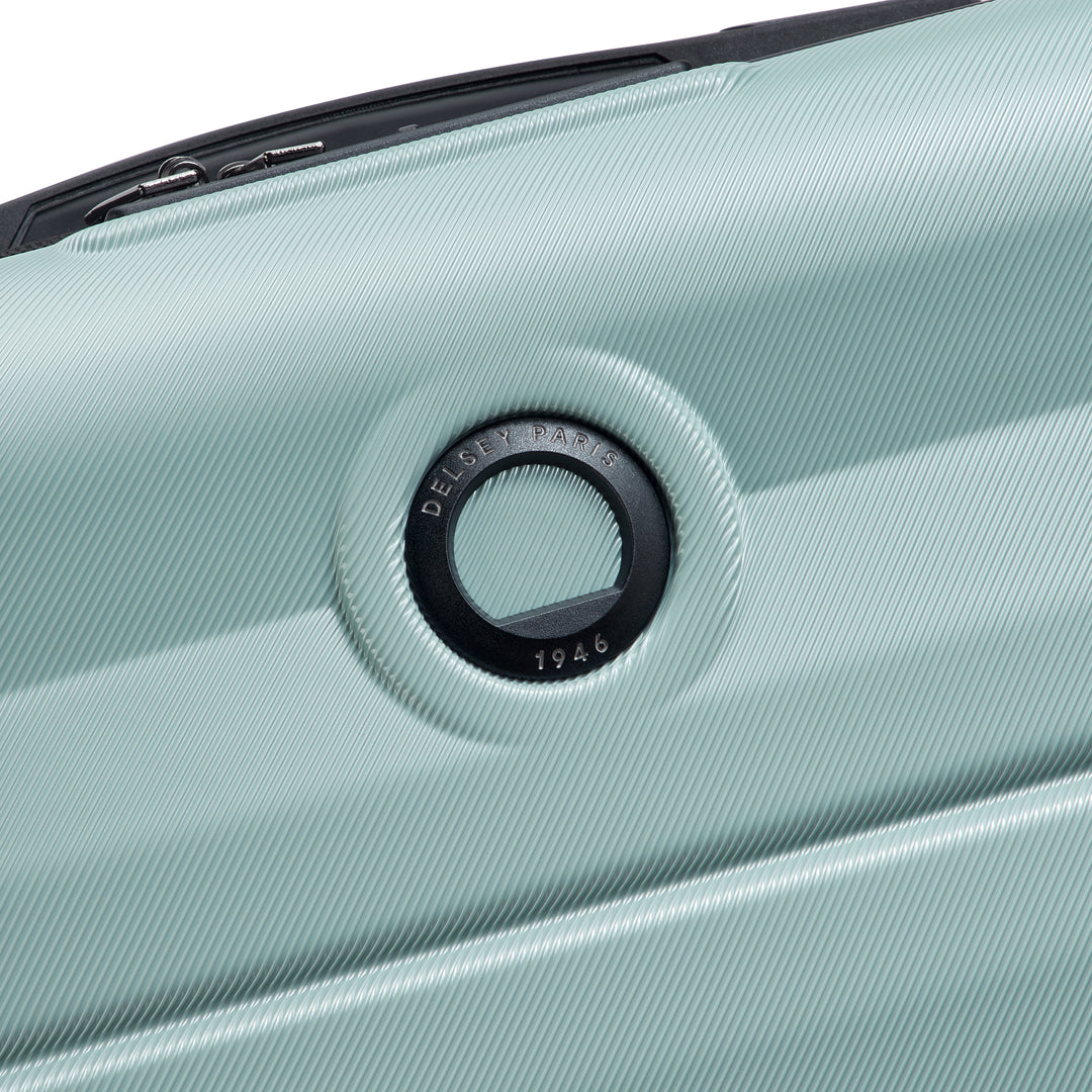 Close-up of a sage green suitcase with a Delsey brand logo on a white background