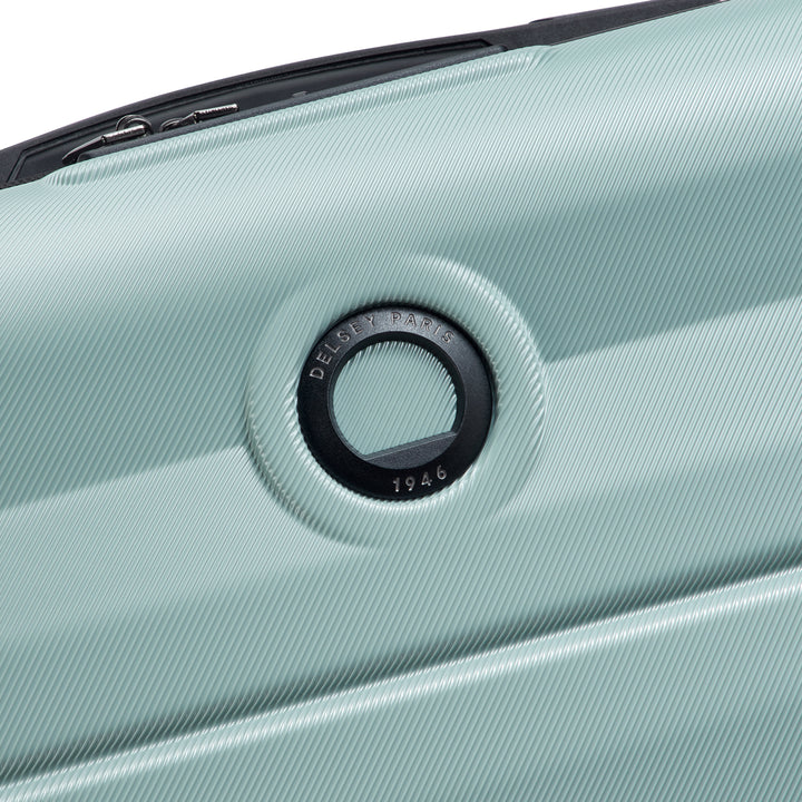 Close-up of a sage green suitcase with a Delsey brand logo on a white background