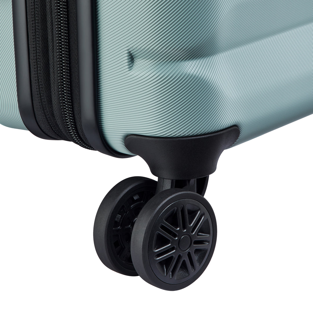 Close-up of a black suitcase wheel on a sage green suitcase with a white background