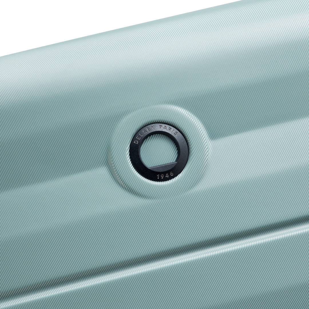Close-up of a sage green suitcase with a Delsey brand logo on a white background